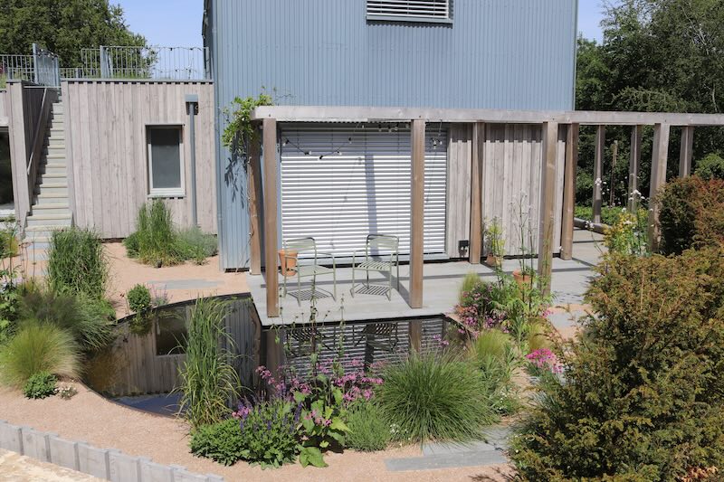 Modern landscaped garden with pond, timber pergola and planting